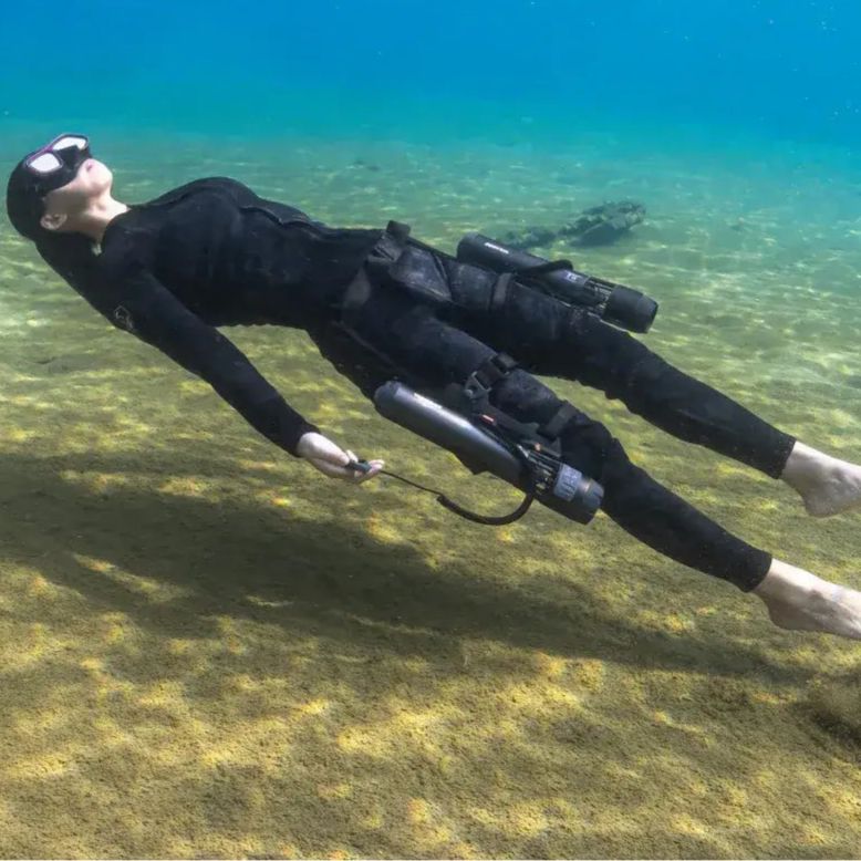 Person in a black wetsuit and subnado floating in clear water.